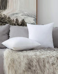 Weiße Kissen auf grauem Sofa mit Felldecke und Waldbild im Hintergrund